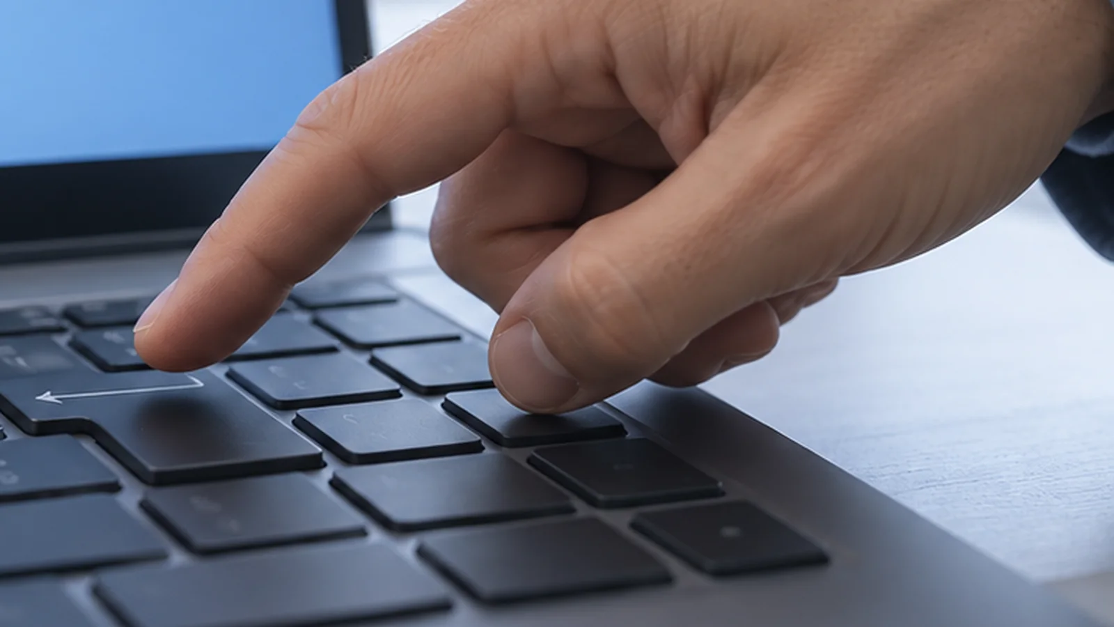 Close view of a hand poised at a computer keyboard beneath a screen.